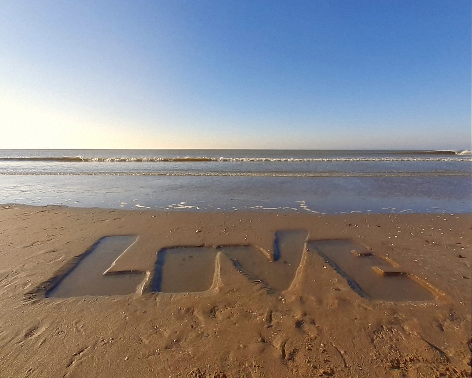 lettrage love creusé dans le sable d'une plage, la mer au loin